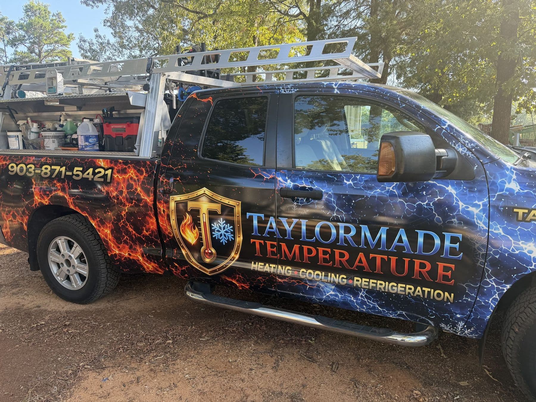 A wrapped TaylorMade Temperature service truck parked at a job site, side view, with trees behind it